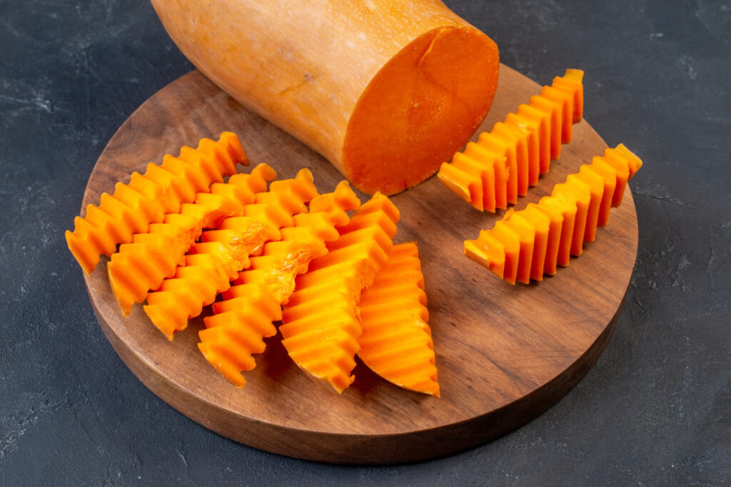 uma mão usando uma faca para descascar cenoura com faca sobre uma tábua de madeira rústica.